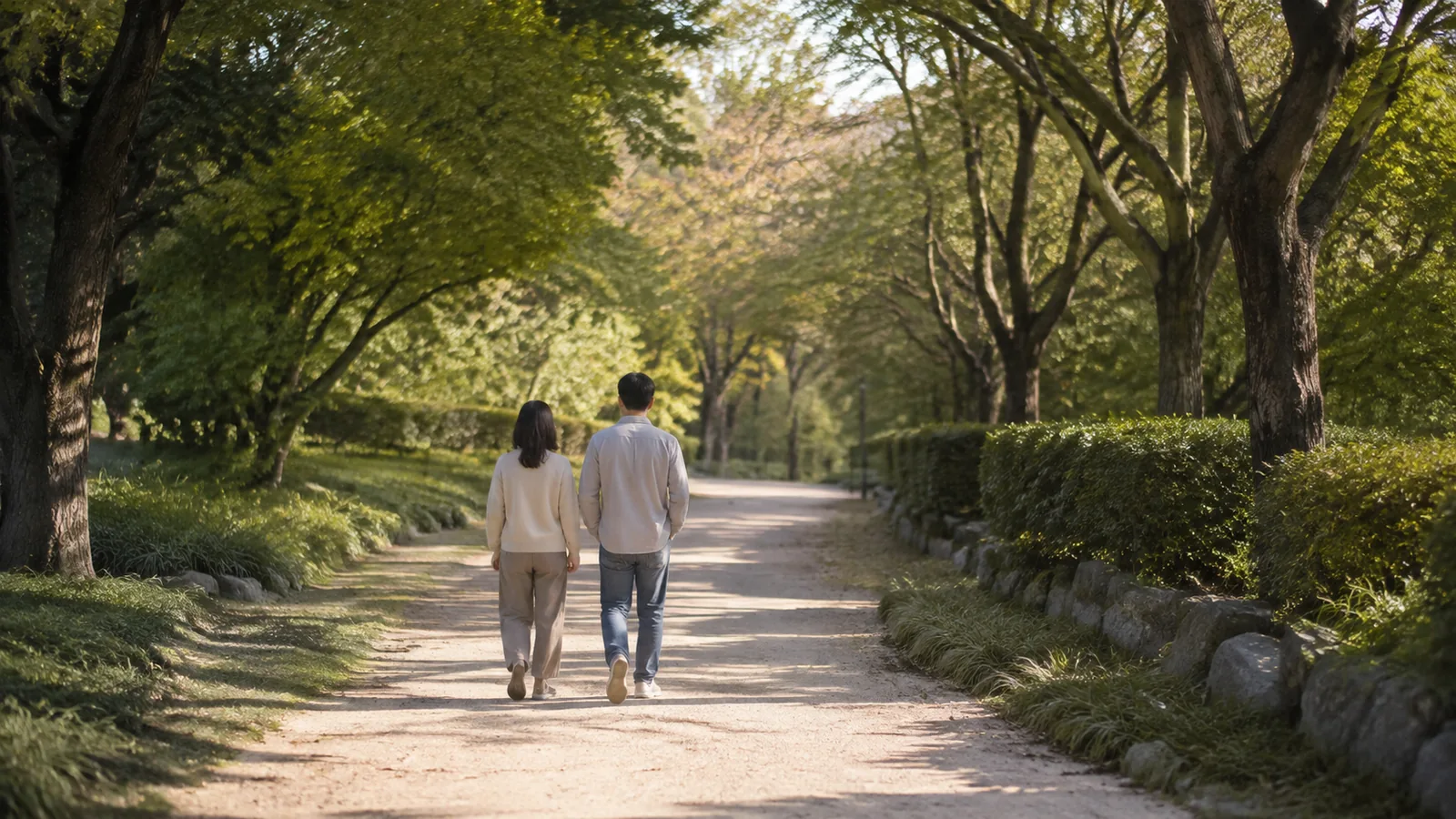 나무 사이로 이어지는 길을 함께 걸어가는 두 사람의 뒷모습